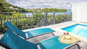 Un área de piscina con dos sillas de descanso, un jacuzzi pequeño y vistas a un lago y colinas.