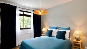 Une chambre à coucher avec un grand lit, deux tables de chevet avec des lampes, une fenêtre avec des rideaux et un luminaire suspendu.