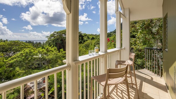 Un balcon avec une table et des chaises, donnant sur un paysage verdoyant et luxuriant et sur un ciel dégagé.