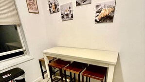Uma cozinha compacta com bancada branca, três banquetas de madeira e um cesto de lixo preto.