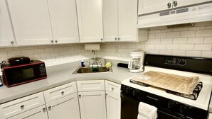 Cozinha compacta com armários brancos, micro-ondas, cafeteira e fogão.