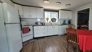 A compact kitchen with white cabinets, a microwave, a coffee maker, and a dining table with a red tablecloth.