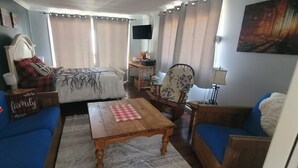 A cozy living room with a bed, blue sofas, a wooden coffee table, and a television on a stand.