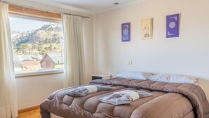 A bedroom with a large bed, a nightstand, a window with curtains, and wall art. - ORIPLATA (Caviahue)