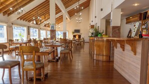 A spacious restaurant with wooden floors and high ceilings, featuring multiple dining tables and chairs, a bar area, and large windows allowing natural light. - ORIPLATA (Caviahue)