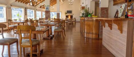 Ein geräumiges Restaurant mit Holzböden und hohen Decken, das mehrere Esstische und Stühle, eine Bar und große Fenster mit Tageslicht bietet.