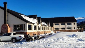 A row of buildings with a snow-covered ground, a white car, and a quad bike parked in front. - ORIPLATA (Caviahue)