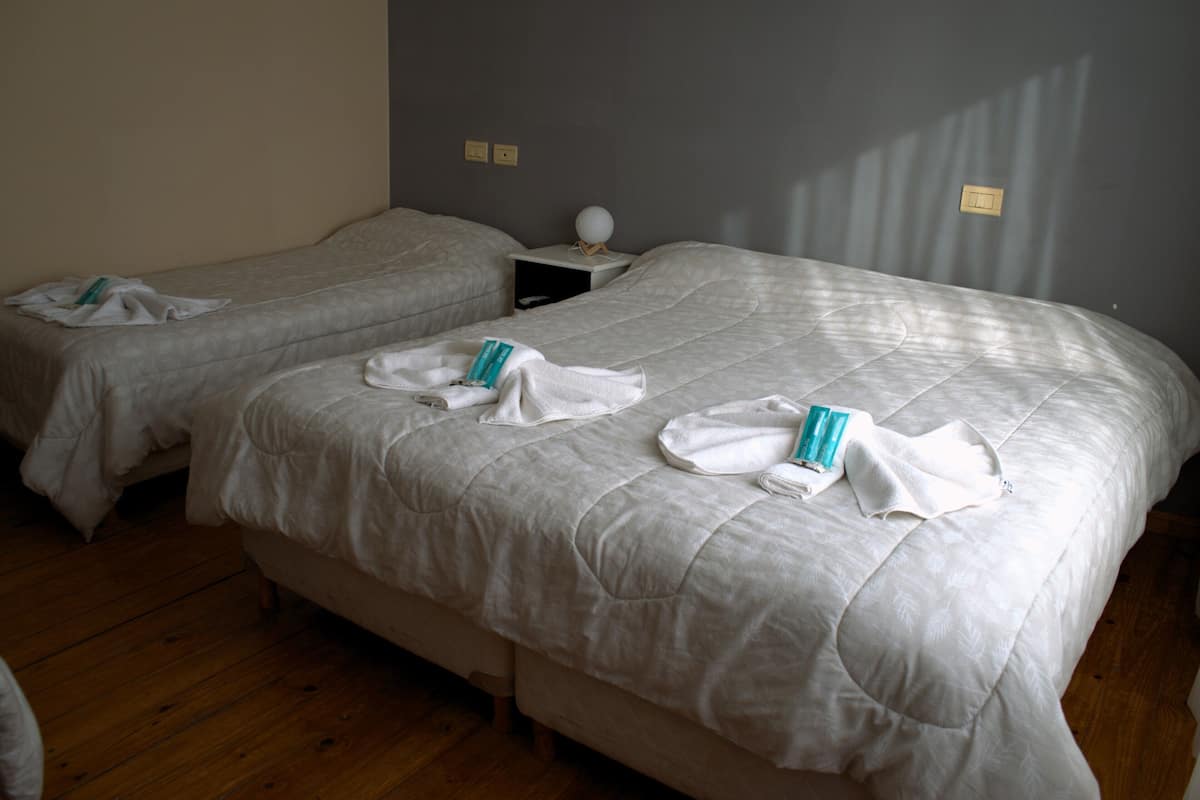 Duas camas de solteiro com roupa de cama branca, uma mesa de cabeceira com abajur e um criado-mudo.