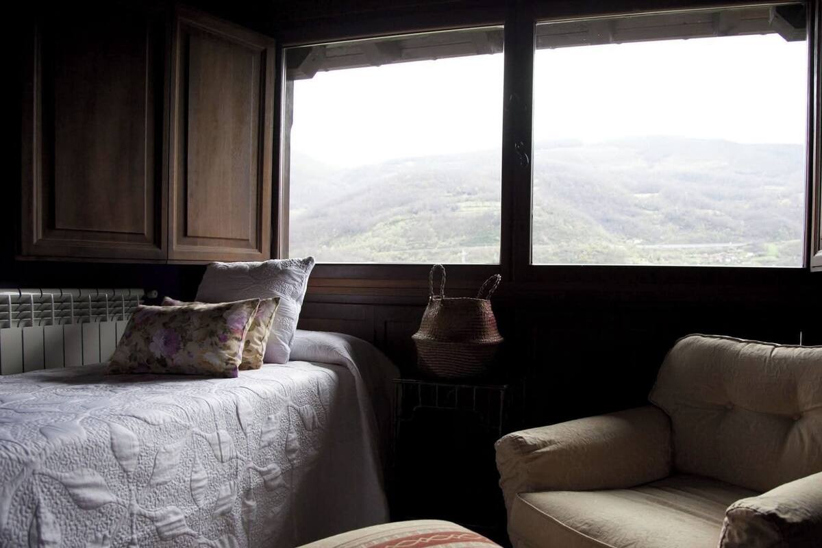 Een slaapkamer met een bed, een stoel en uitzicht op een bergachtig landschap door een raam.