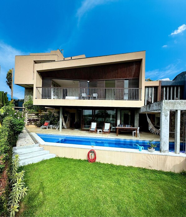 Ein modernes, zweistöckiges Haus mit Swimmingpool, einem Balkon mit Sitzgelegenheiten und einem gepflegten Rasen.