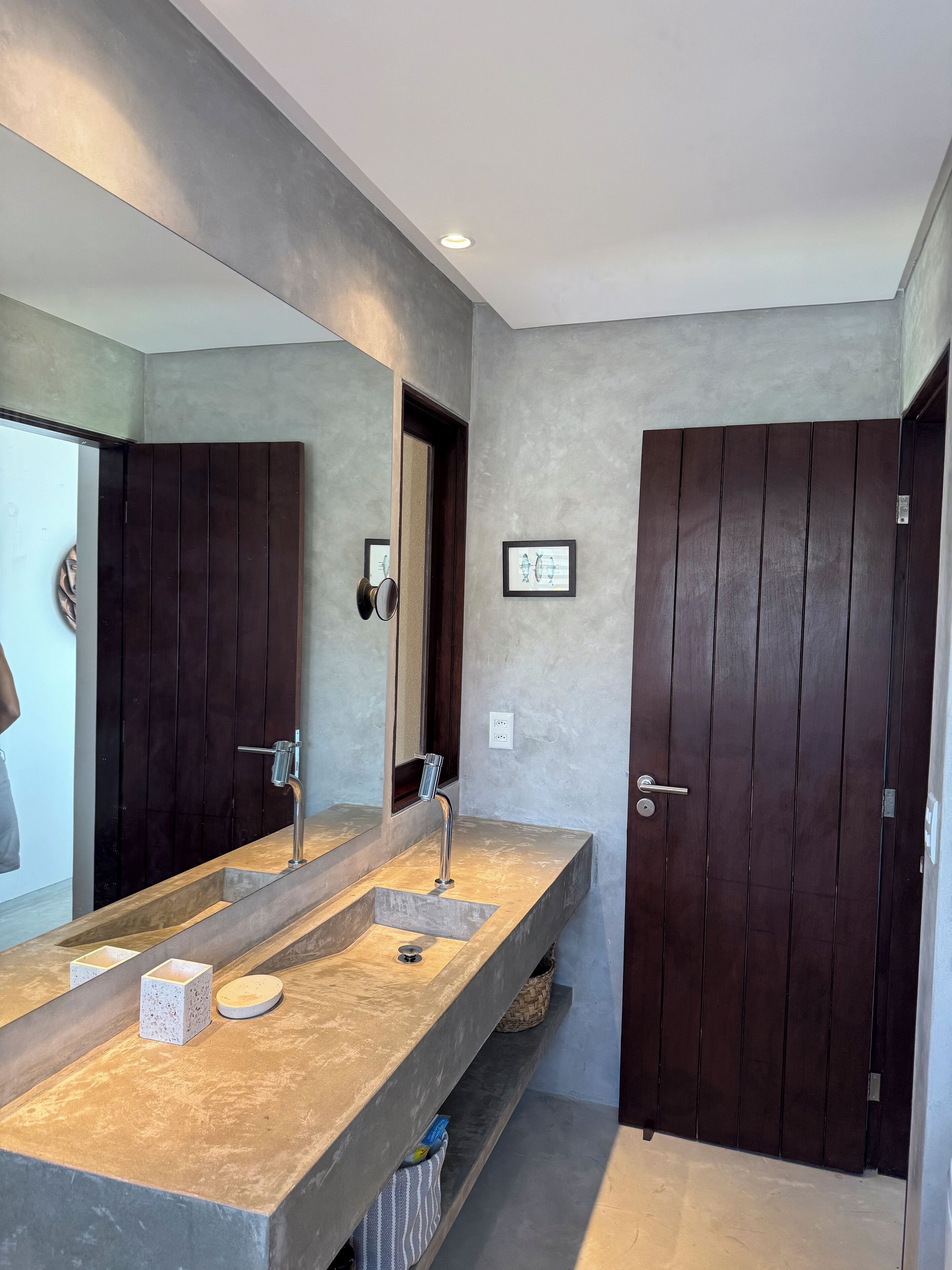 A modern bathroom with a large mirror, two sinks, and a dark wooden door.