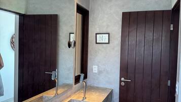 A modern bathroom with a large mirror, two sinks, and a dark wooden door.