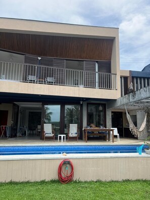 Ein modernes, zweistöckiges Haus mit Swimmingpool, Sitzgelegenheiten im Freien und einer Hängematte.