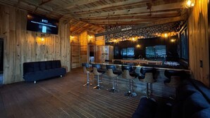 Interior de madeira acolhedor, com área de bar, assentos e uma tela de televisão.