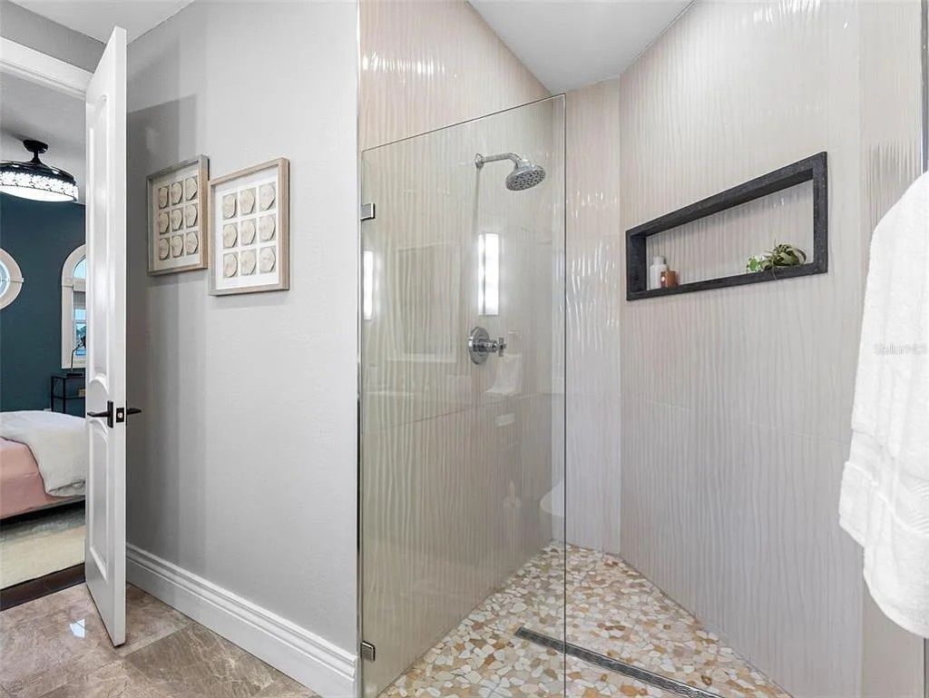 A modern bathroom with a glass shower enclosure, a small shelf with toiletries, and a framed picture on the wall.