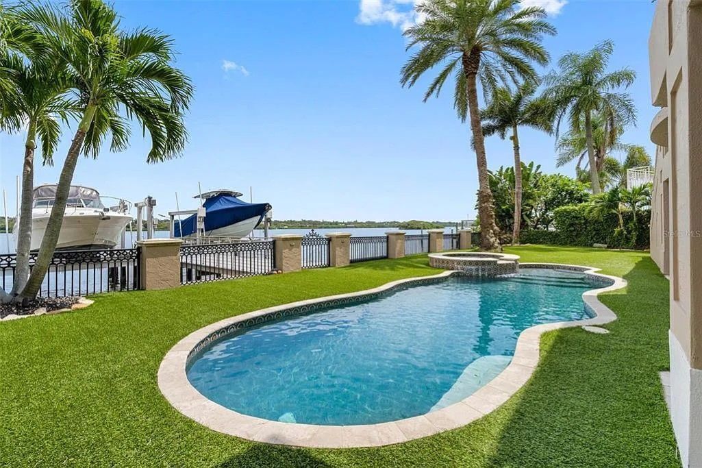 Una piscina de borde curvo, rodeada de césped cuidado y palmeras.