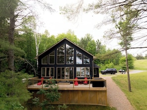 A modern cabin with a large deck, surrounded by trees.
