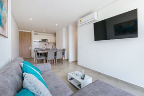 Een moderne woonkamer met een grijze bank, een salontafel en een flatscreen televisie aan de muur.
