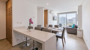 A modern dining area with a long table, chairs, and a view of the cityscape through large windows. - U-GO Edificio Salguero Sunset (Santa Marta)