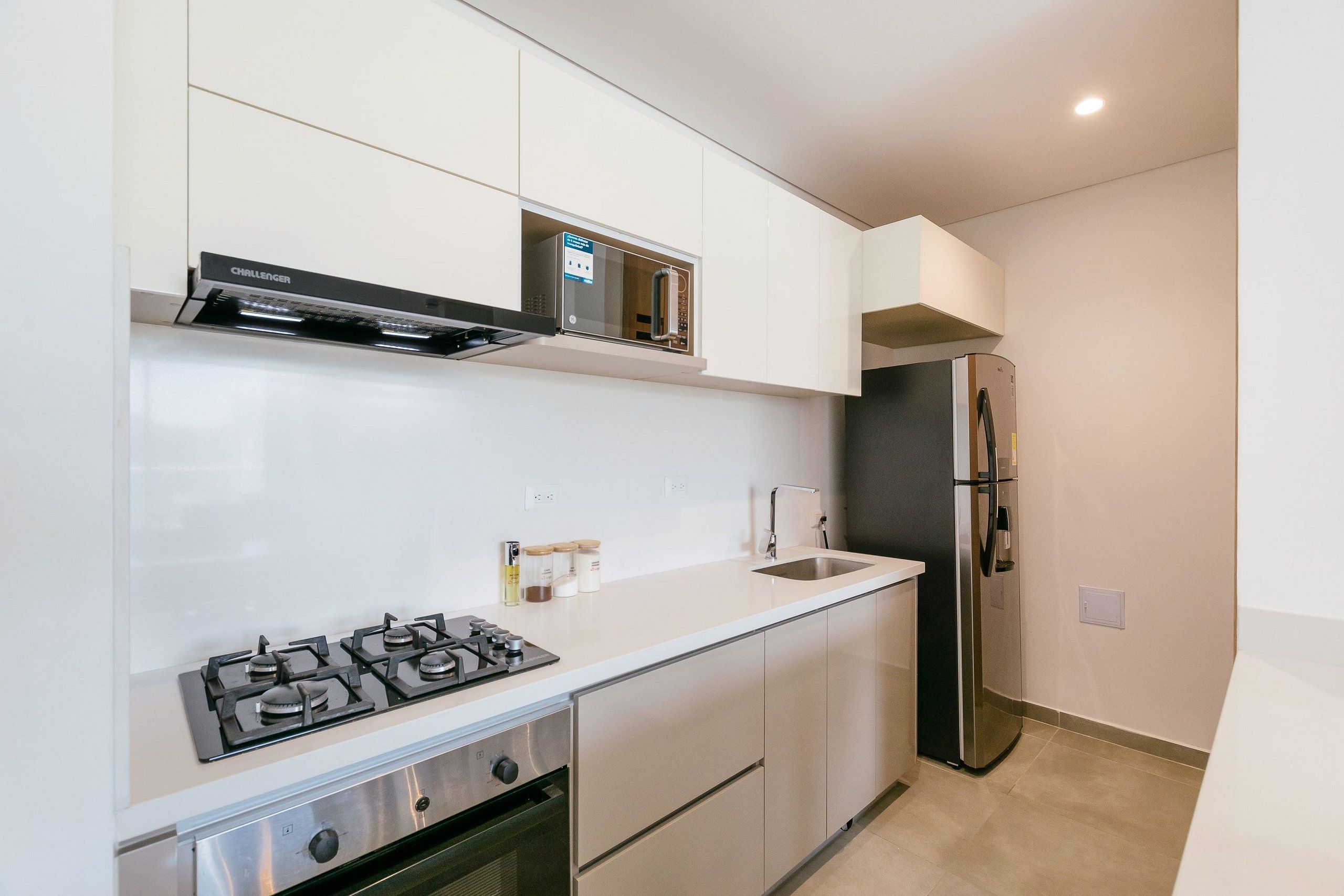 Una cocina moderna con estufa a gas, horno, refrigerador de acero inoxidable y alacenas blancas.