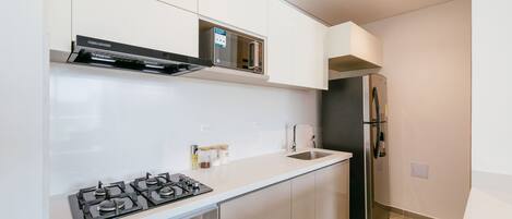 A modern kitchen with a gas stove, oven, stainless steel refrigerator, and white cabinetry.