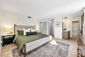 A bedroom with a bed, bedside tables, a nightstand, a dresser, a mirror, and a door leading to a bathroom. - Pool-Fenced Yard-Pool Table-Sleeps 10 (Fairfield)