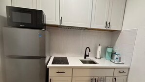 A compact kitchen with white cabinets, a stainless steel refrigerator, a microwave, a sink, and a striped rug. - Cozy Studio - Centrally Located - Free Parking (Orlando)