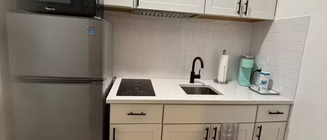 A compact kitchen with white cabinets, a stainless steel refrigerator, a microwave, a sink, and a striped rug.