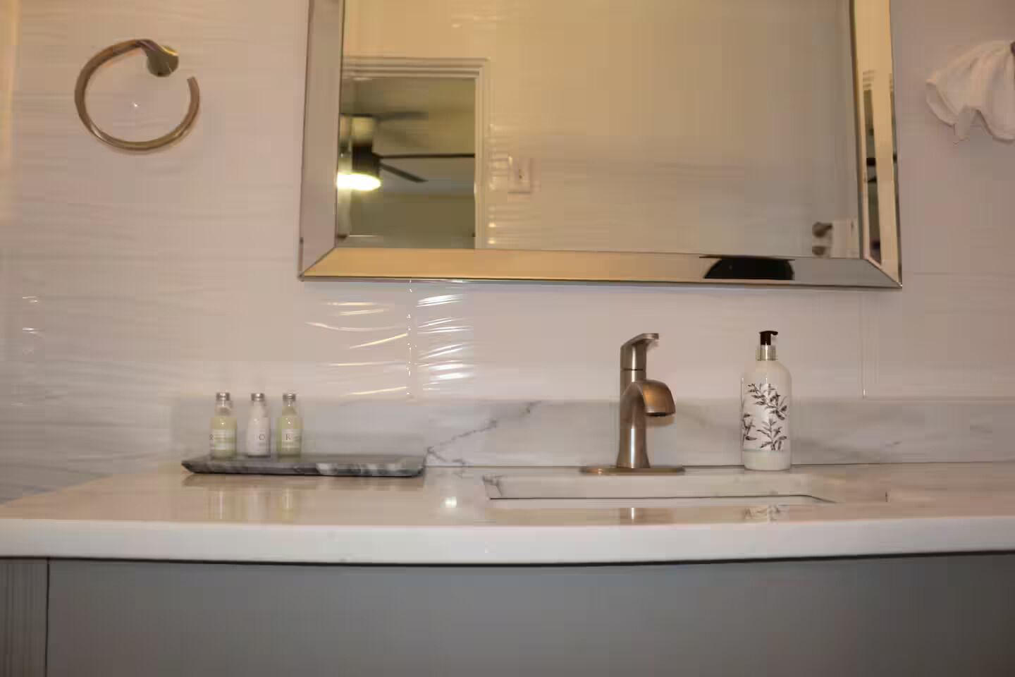 A bathroom with a white marble sink, a gold faucet, and a mirror above it. There are three bottles of liquid soap on the sink.