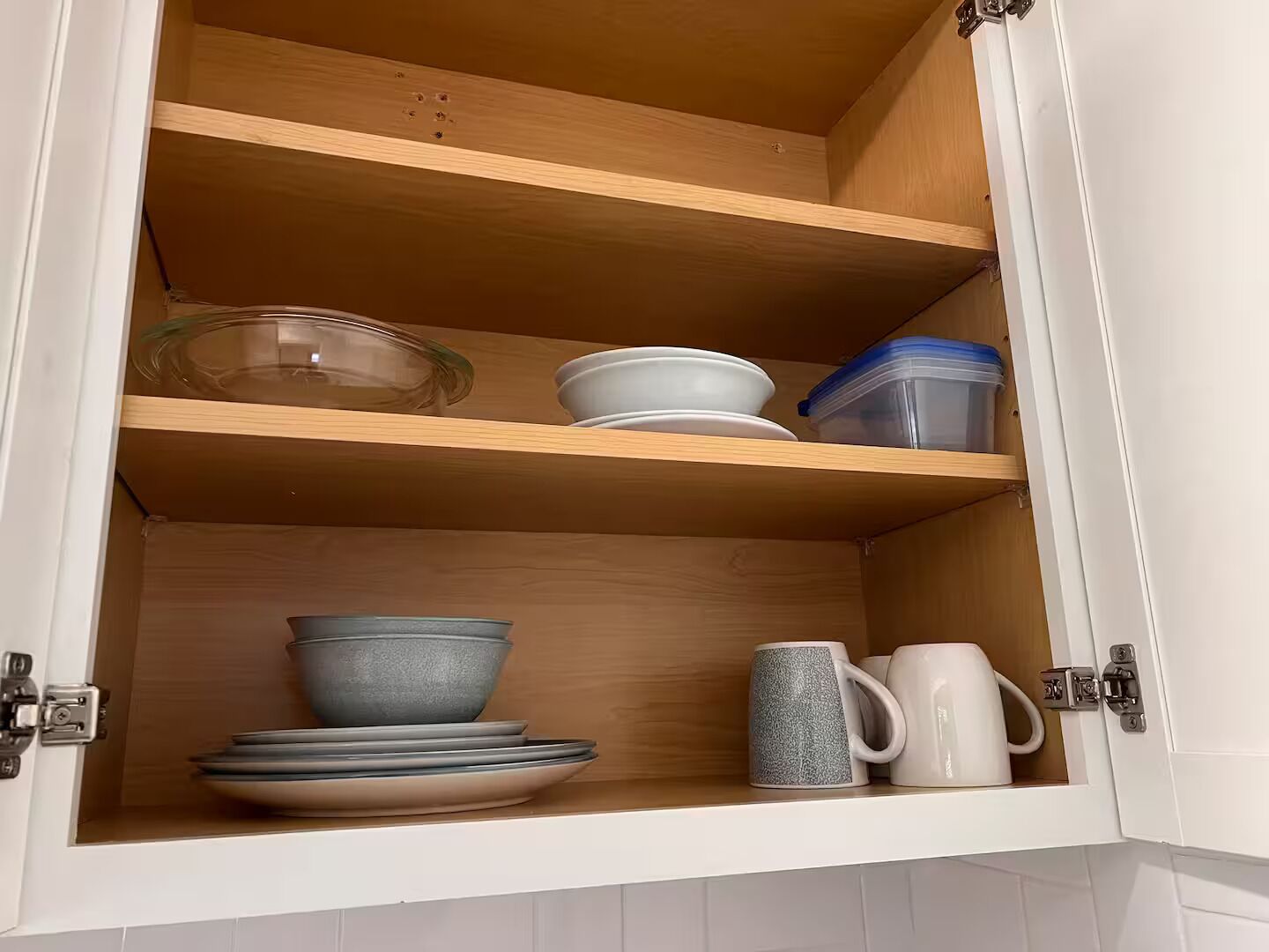 A kitchen cabinet with wooden shelves, containing bowls, plates, and a mug.