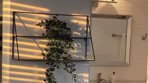 A bathroom with a mirror, sink, and a plant in a black metal planter. - Cozy Studio - Centrally Located - Free Parking (Orlando)