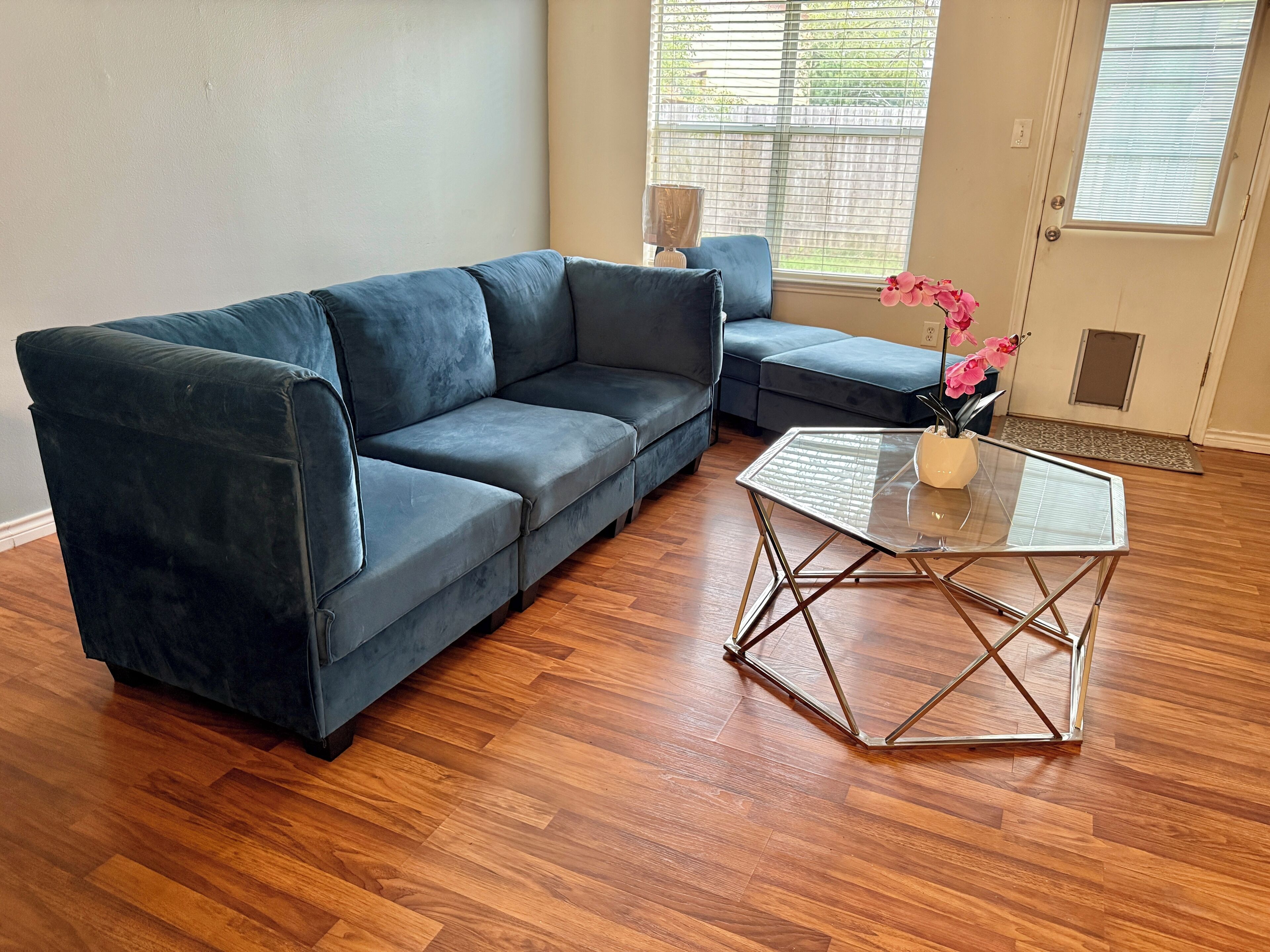 Ein Wohnzimmer mit einem dunkelblauen Sofa, einem Glastisch und einem kleinen Beistelltisch mit rosa Blumen.