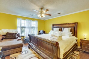 A bedroom with a large bed, a ceiling fan, and a window with curtains.