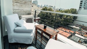 Een balkon met een witte bank, een houten tafel en een witte fauteuil.