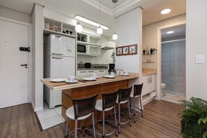 A modern kitchen with a central island, bar stools, white cabinetry, and a microwave.