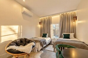 A hotel room with two beds, a chair, a table, and an air conditioning unit. - Studio Retreat | Near Woodbury Commons & Legoland (Monroe)