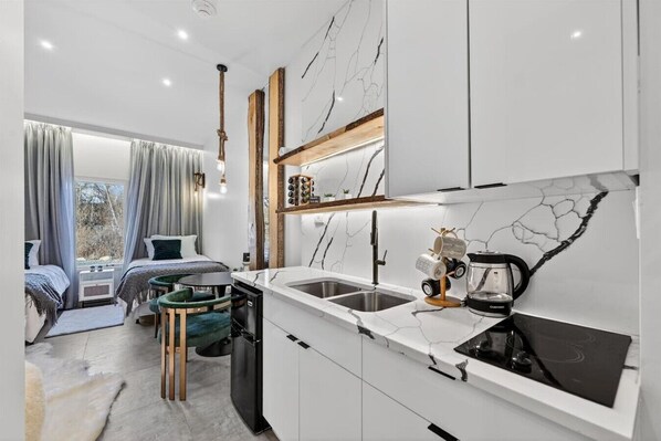 A compact hotel room with a kitchenette, a dining area, and a bed with a view.