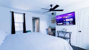 A bedroom with a large bed, a ceiling fan, a TV mounted on the wall displaying streaming services, and a door to another room. - Hidden Gem Near Plaza Mall - Mi Casita McAllen (McAllen)
