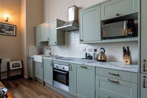 A kitchen with light green cabinets, a stainless steel oven, a microwave, and a kettle on the countertop. - Stylish Quayside Duplex 2Bed Free Parking City Centre Wi Fi (Gateshead)