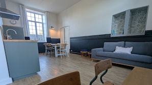 A modern kitchen with a dining area, a grey sofa, and a window with floral artwork. - La Bonne Ecole - La Marelle Vacation Rental - Sleeps 7 - 20 min from Puy du Fou - (Les Landes-Genusson)