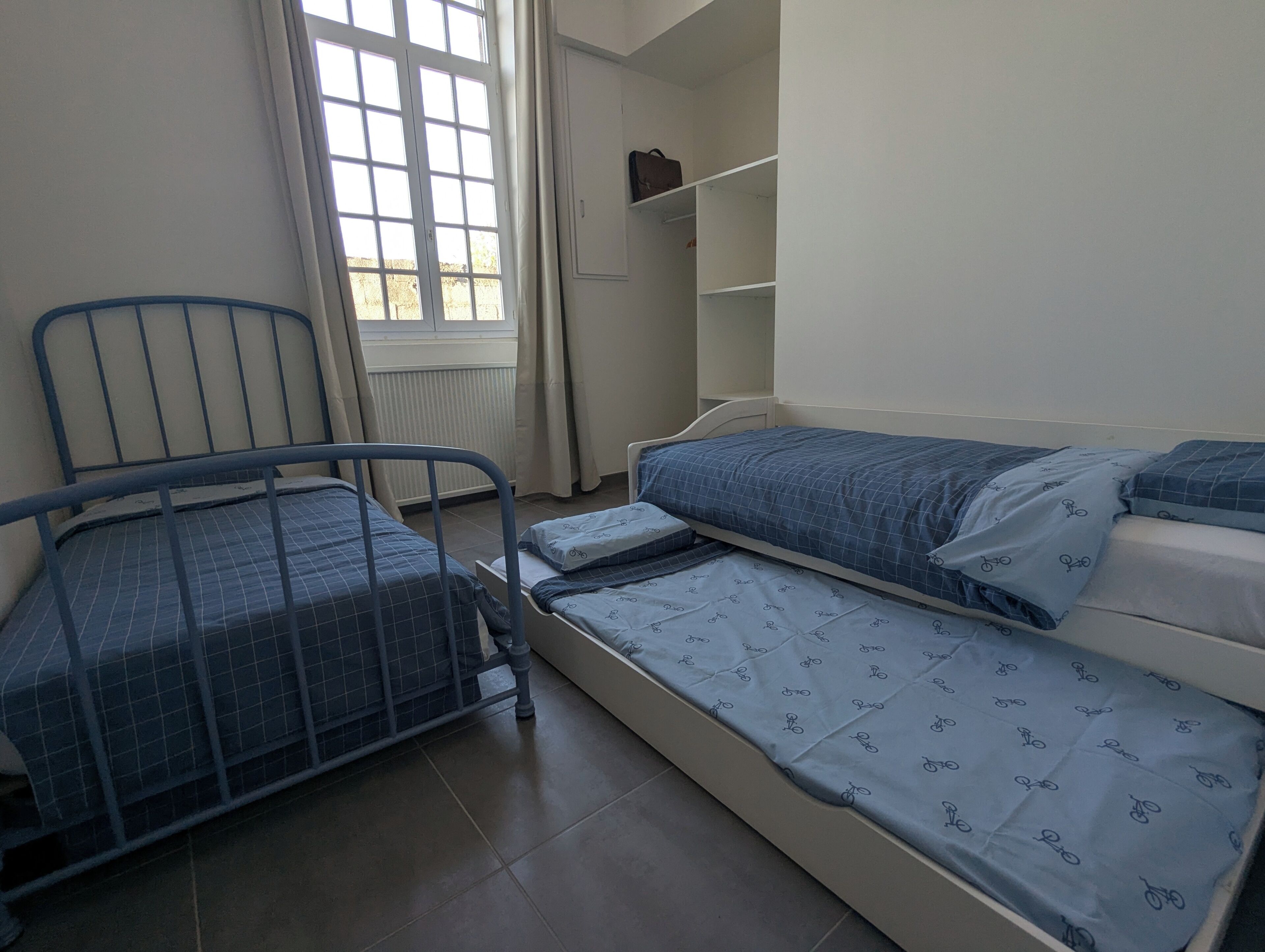 Un dormitorio con dos camas, una ventana, un radiador y un armario.