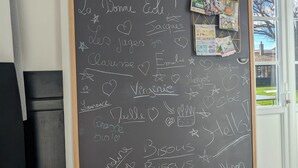 A blackboard with names and hearts, a bulletin board with magazines, and a door with a view of the outside. - La Bonne Ecole - La Marelle Vacation Rental - Sleeps 7 - 20 min from Puy du Fou - (Les Landes-Genusson)