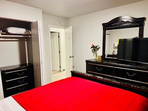 A bedroom with a red bedspread, a black dresser with drawers, a large mirror, and a white door leading to another room. - Close to everything you need Unit B Entire rental unit in Fairbanks, Alaska (Fairbanks)