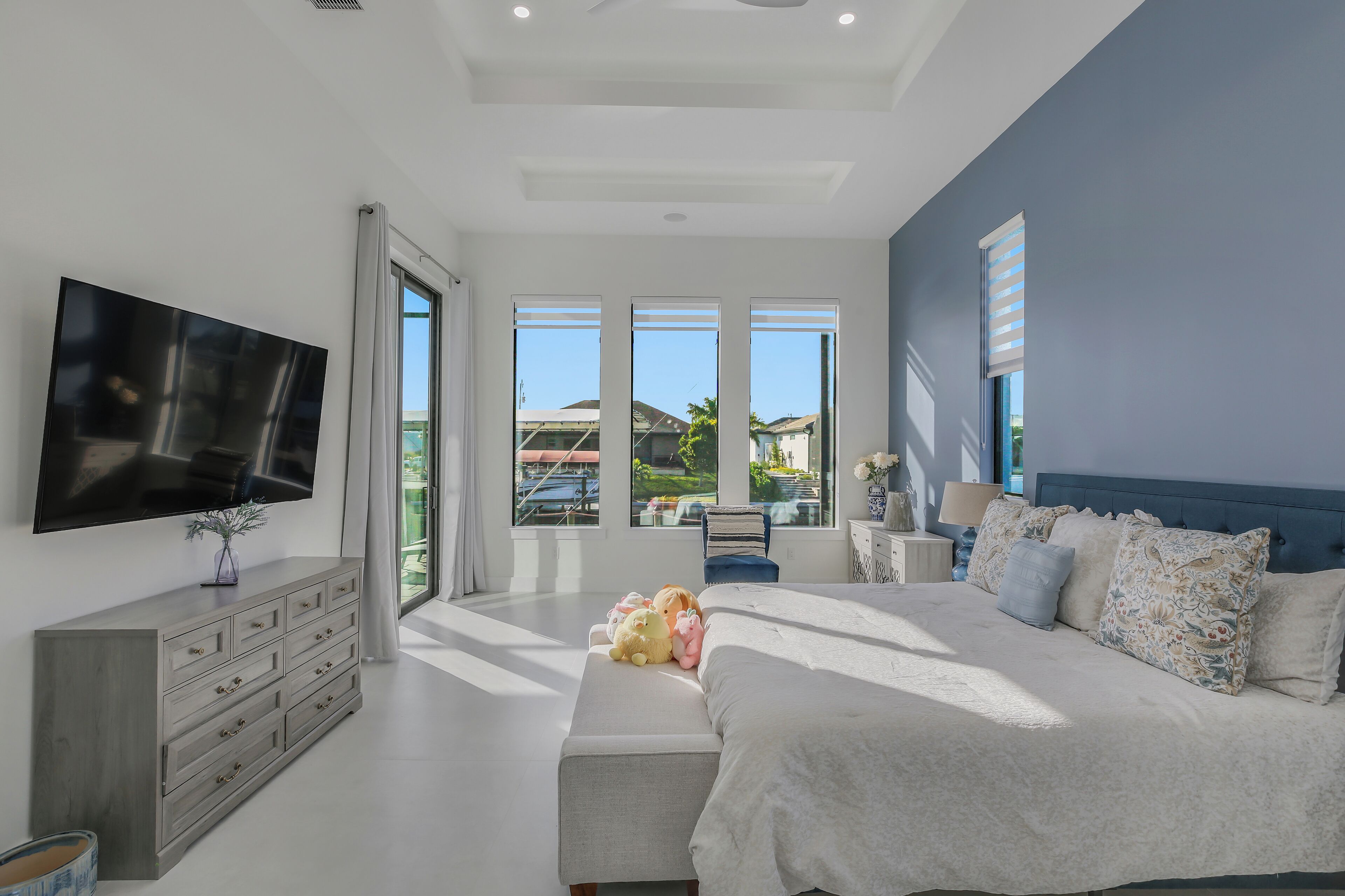 A modern bedroom with a large bed, a flat-screen TV, and a view of the outdoors.