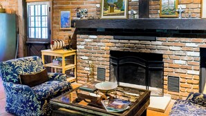 Ein gemütliches Wohnzimmer mit Kamin aus Backsteinen, einem Holztisch und blau gemusterten Sofas.
