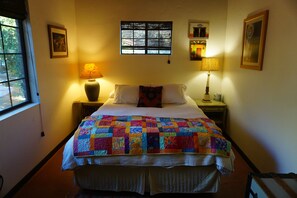 A neatly made bed with a colorful quilt, two bedside lamps, a window with blinds, and a small shelf with a lamp. - Spacious Orchard Farmhouse in Quiet Canyon (Dudleyville)