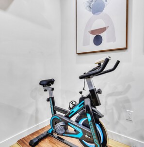 Ein stehendes Fitnessrad in einem Raum mit weißer Wand und einem gerahmten abstrakten Gemälde.