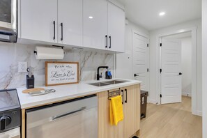 A modern kitchen with white cabinets, a marble backsplash, a stainless steel dishwasher, and a sink with a faucet. - Stylish Suite by Airport/Fast Wi-Fi/Free Driveway Parking/Sleeps 4/Self Check-in (Calgary)