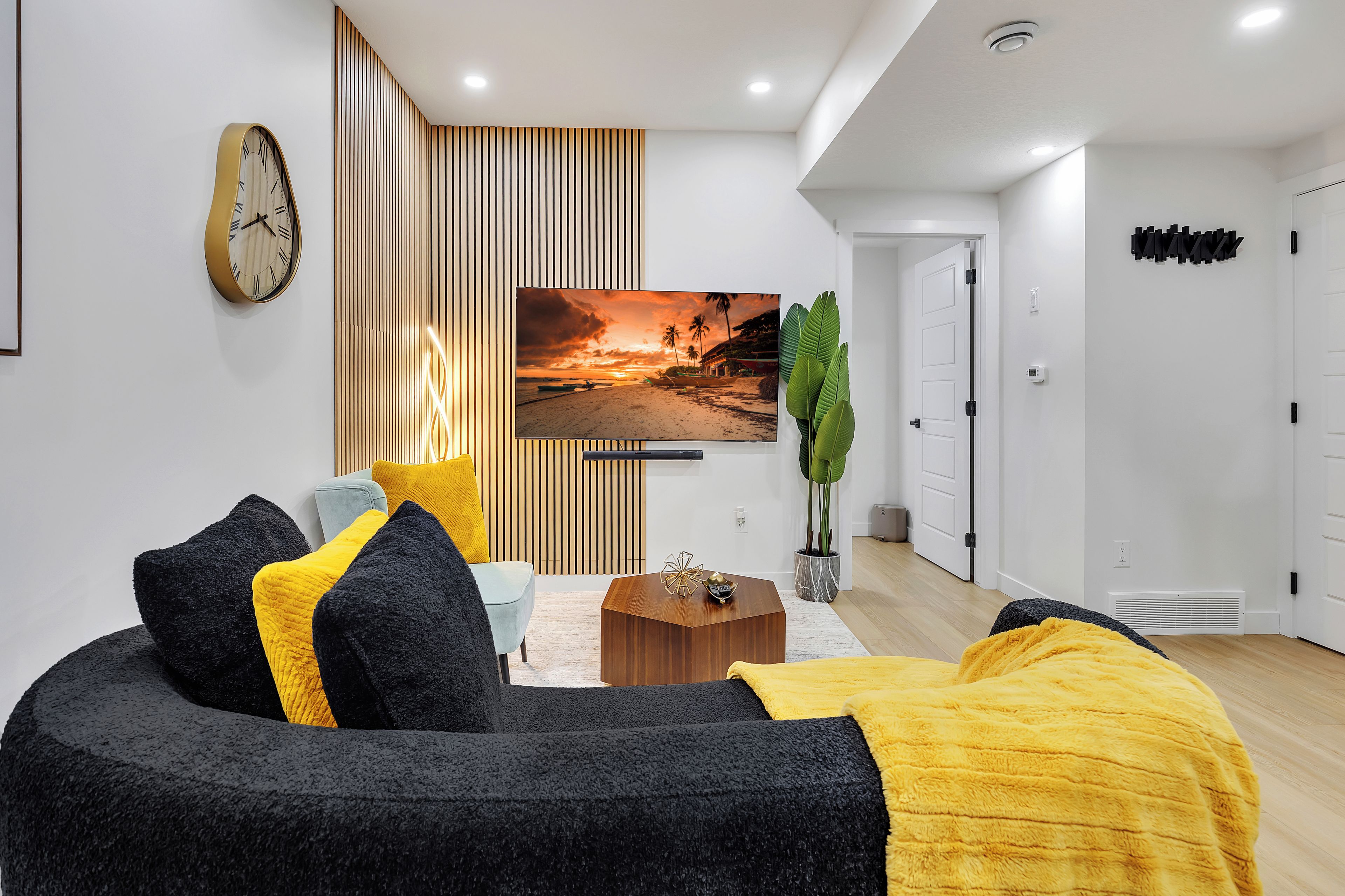 Un salon moderne avec un canapé, une table basse, un téléviseur et une horloge murale.