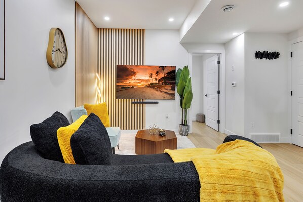 Un salon moderne avec un canapé, une table basse, un téléviseur et une horloge murale.
